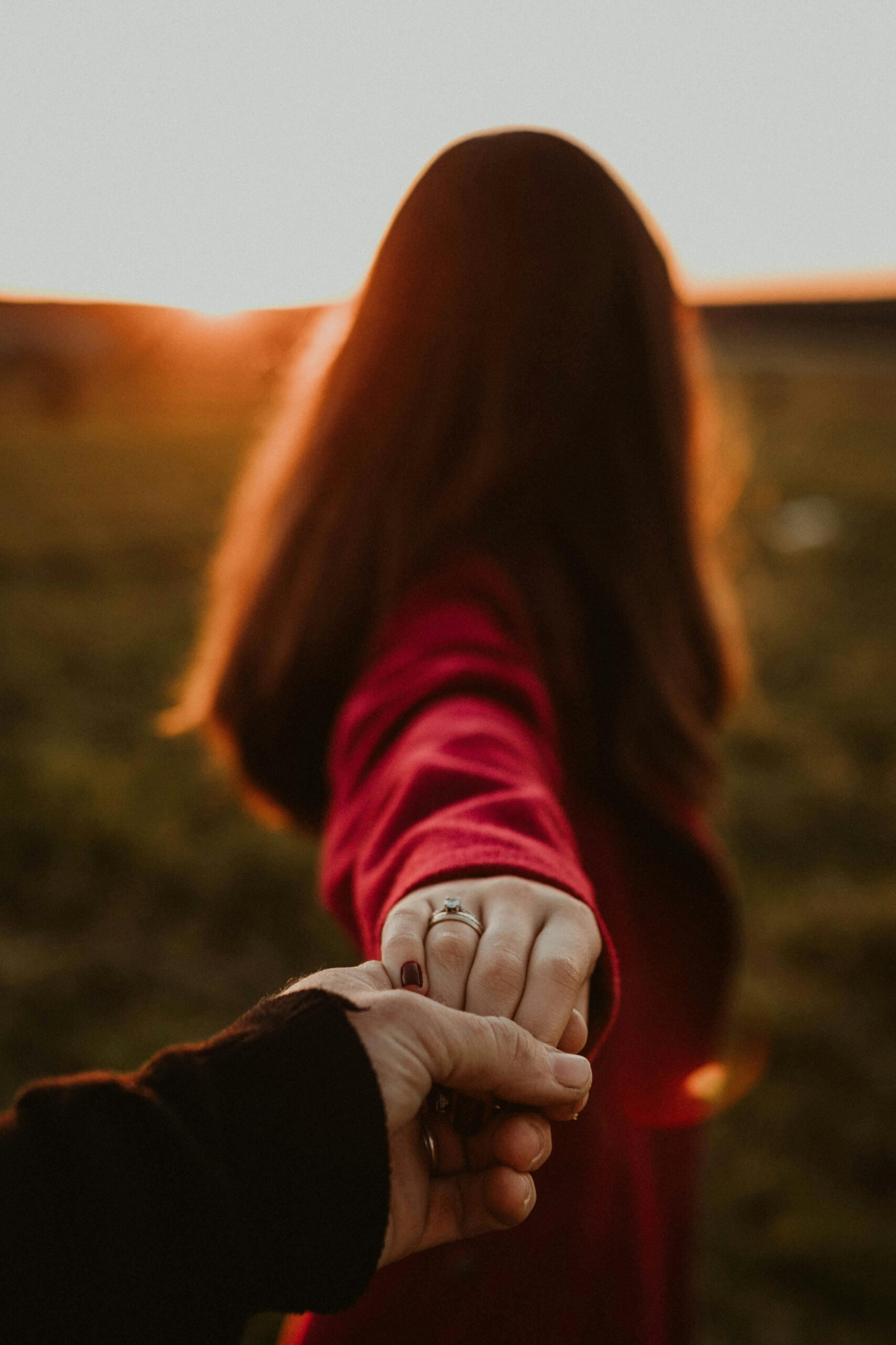A hand reaching back to hold another, walking toward a sunset horizon