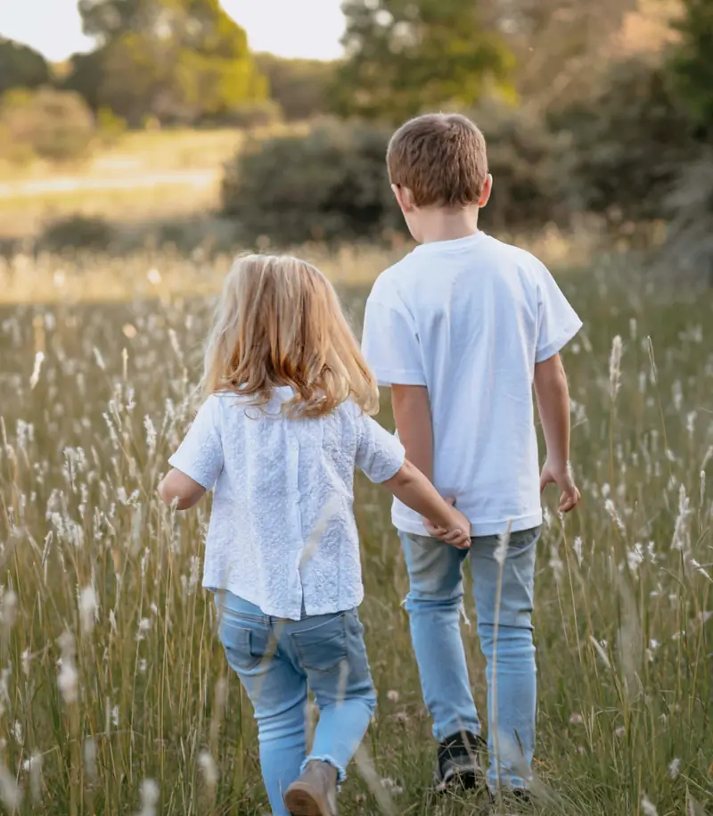 Two children walking together through a sunlit field
